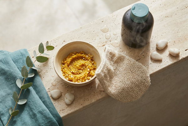 Bowl of golden turmeric and sea salt body scrub with a natural exfoliating mitt on a stone ledge