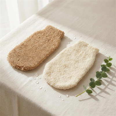 Two natural-fibre exfoliating body mitts, tan and cream, on bone linen with eucalyptus